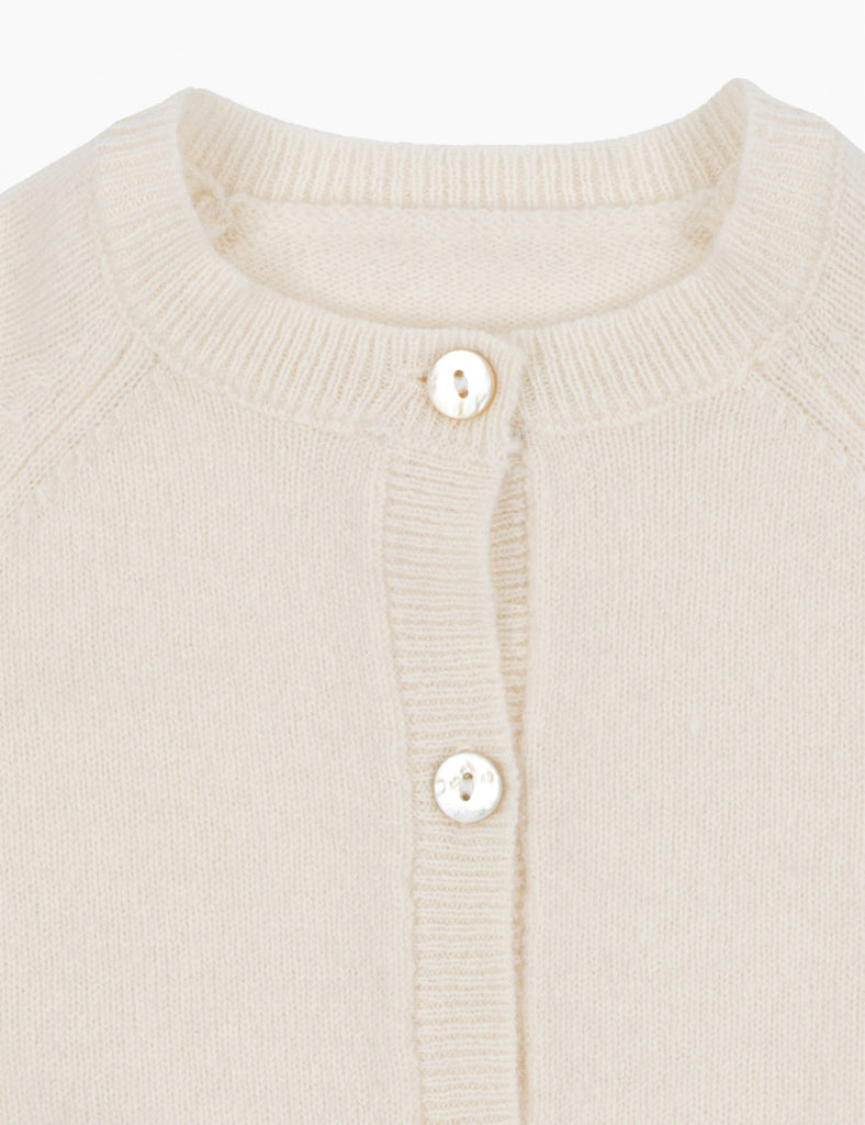Close-up of a cream-colored cardigan with button details on a white background