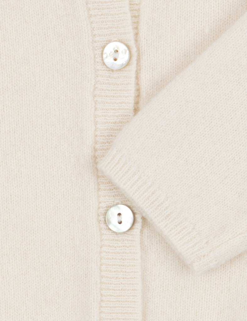 Close-up of a cream-colored cardigan with button details on a light background