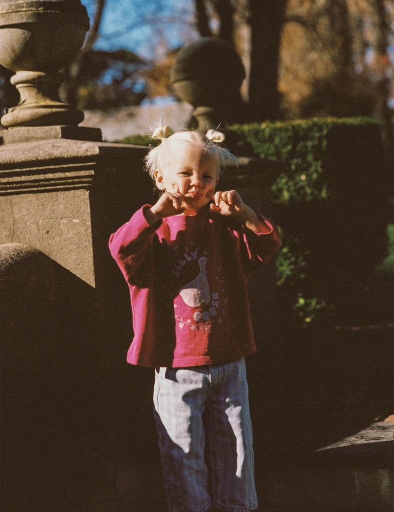 Child in a pink jacket standing outdoors with stone sculptures and greenery in the background