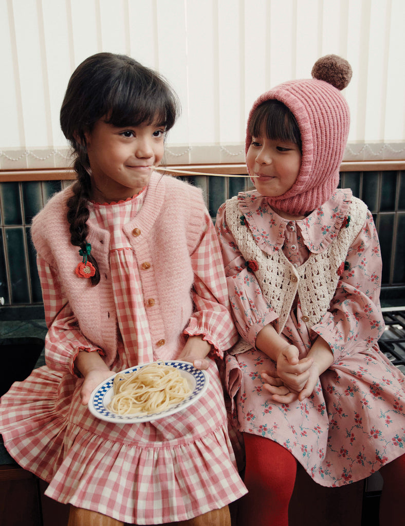 Two young girls in pink and floral dresses sitting next to each other.