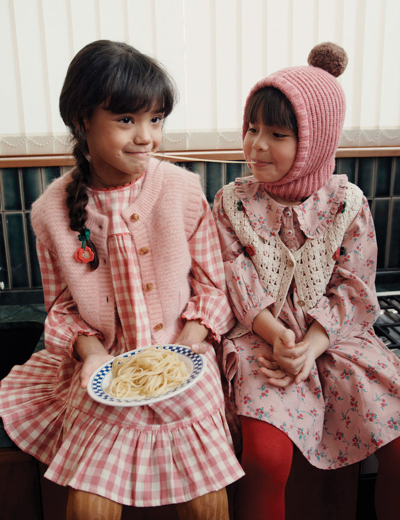Two young girls in pink dresses sitting next to each other, one holding a plate of food.