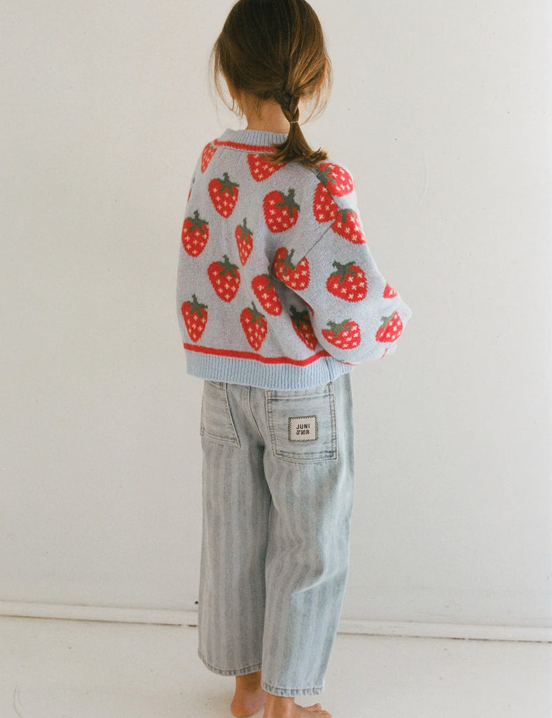 Child wearing a strawberry patterned sweater and jeans against a white background