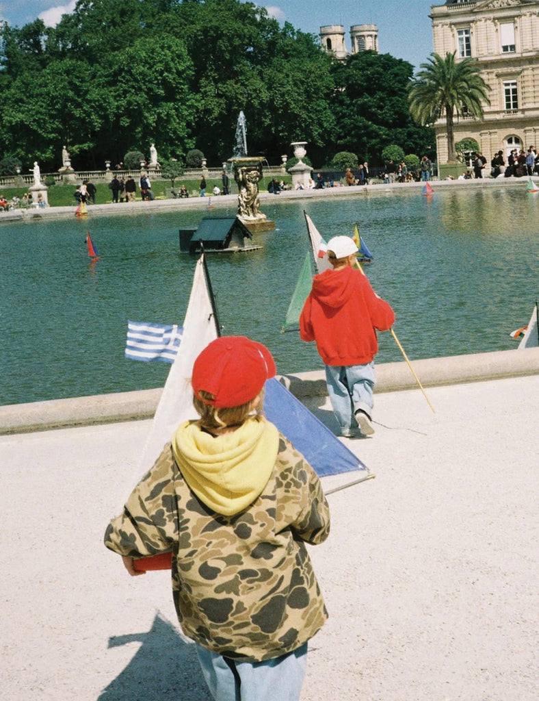 Two children playing with toy boats by a fountain in a park.