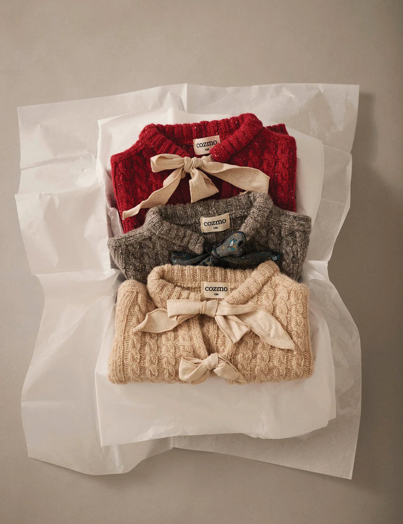 Three knitted sweaters in red, gray, and beige with decorative bows on a white background.