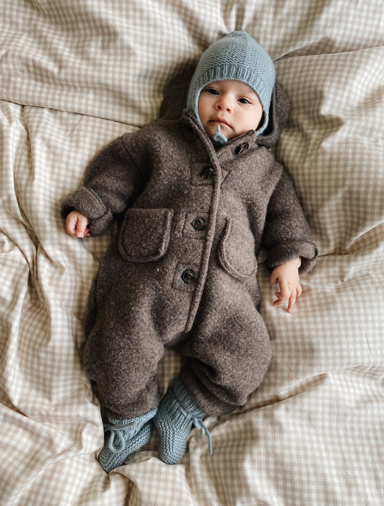 Baby wearing a brown coat and gray hat lying on a checkered blanket