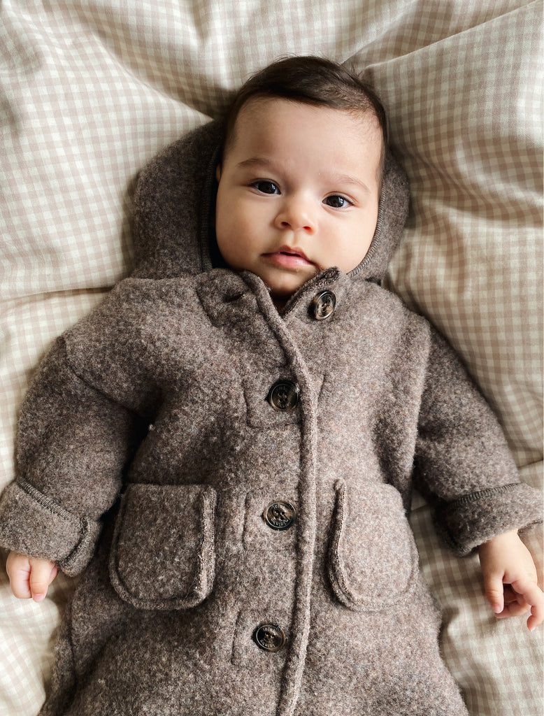 Baby wearing a brown coat lying on a checkered blanket