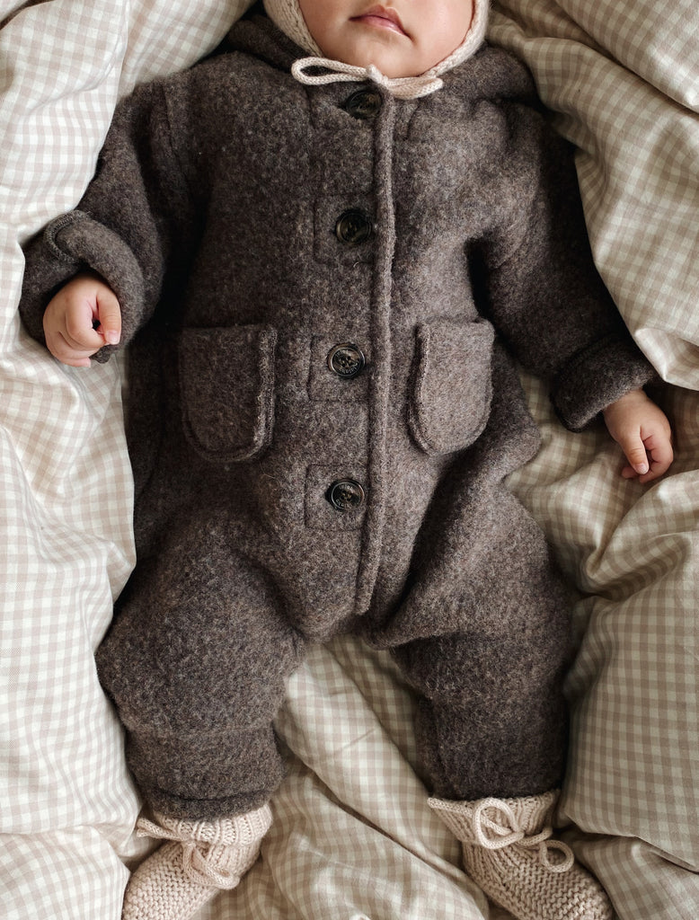 Baby wearing a brown outfit with buttons on a checkered blanket