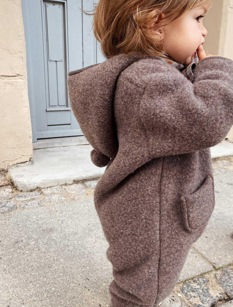 Child wearing a brown hooded coat on a sidewalk.