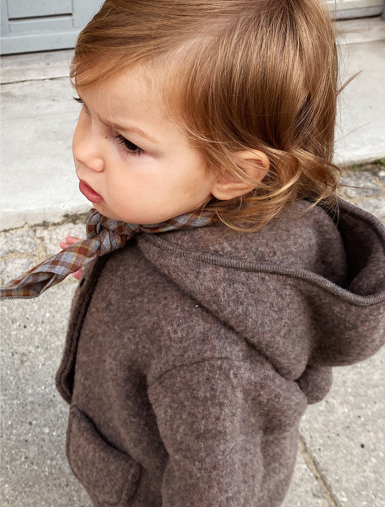 Child wearing a brown coat with a plaid bow tie outdoors.