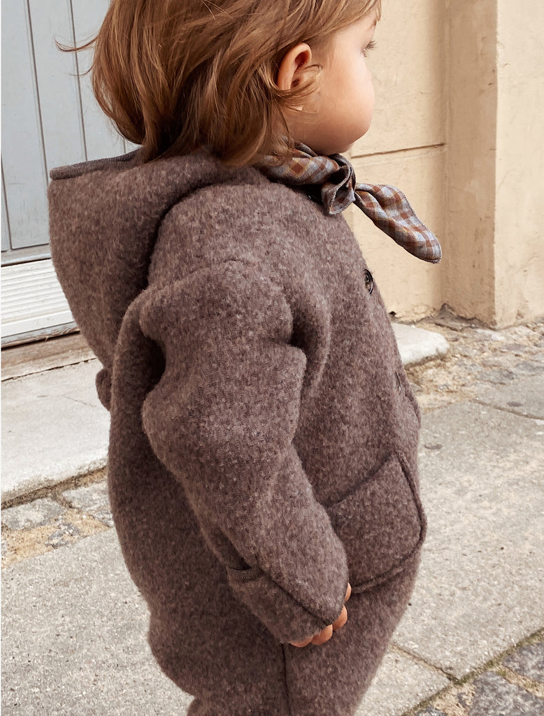 Child wearing a brown coat with a patterned scarf outdoors.