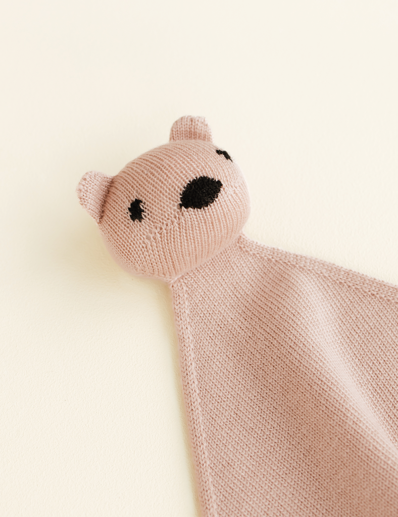 Knitted bear-shaped comfort blanket on a light beige background