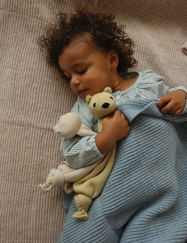 Child holding a teddy bear and wrapped in a blanket on a textured surface