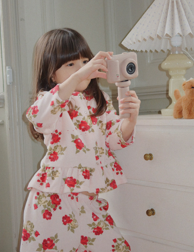 Child in floral pajama set taking a mirror selfie with a pink camera.
