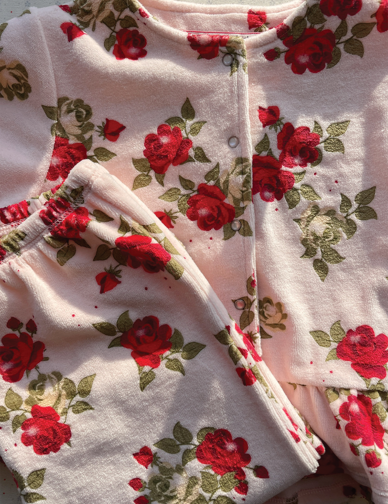 Floral patterned fabric with red roses and green leaves on a light pink background
