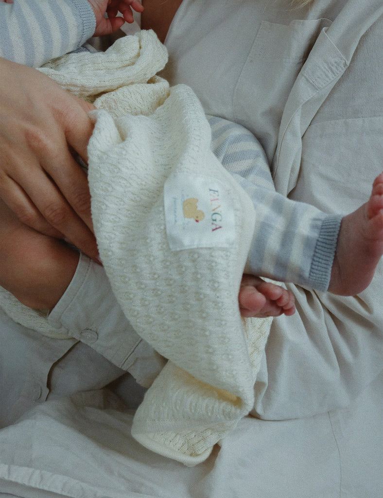 Baby being held by an adult wearing the venti knit pants in gray dawn, wrapped in a blanket.