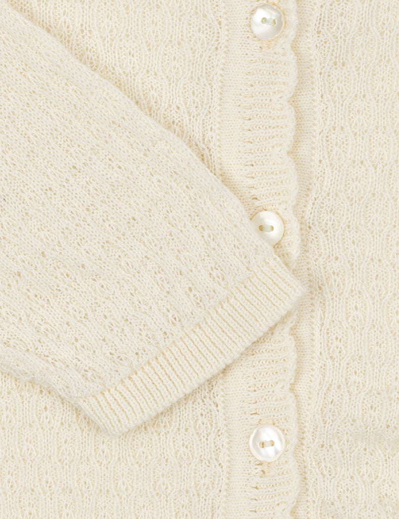 Close-up of a cream-colored cardigan with pearl buttons on a matching background