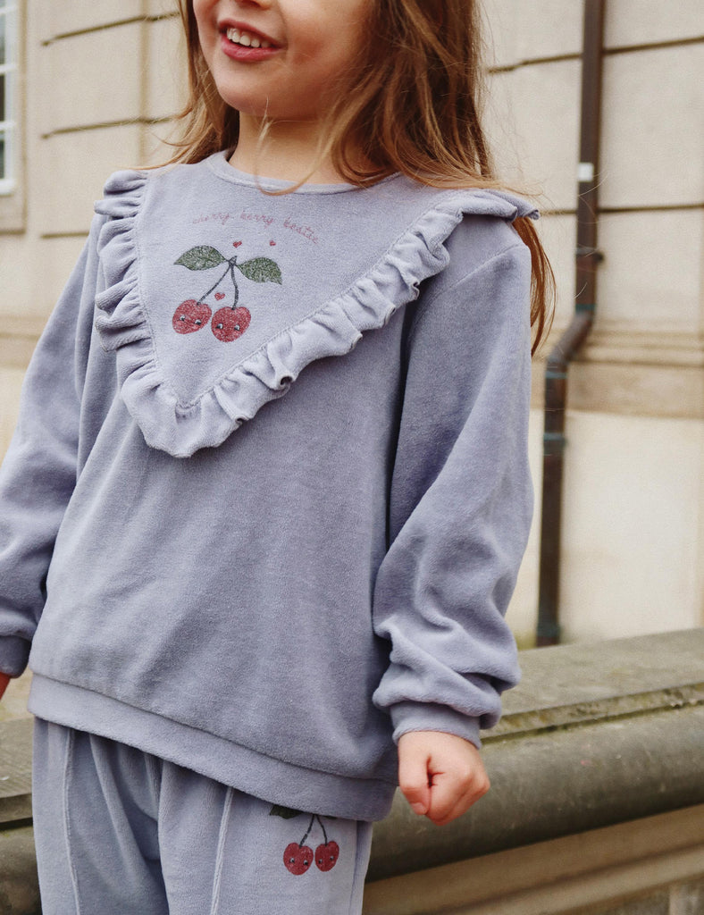 Child wearing a light purple outfit with cherry designs outdoors.