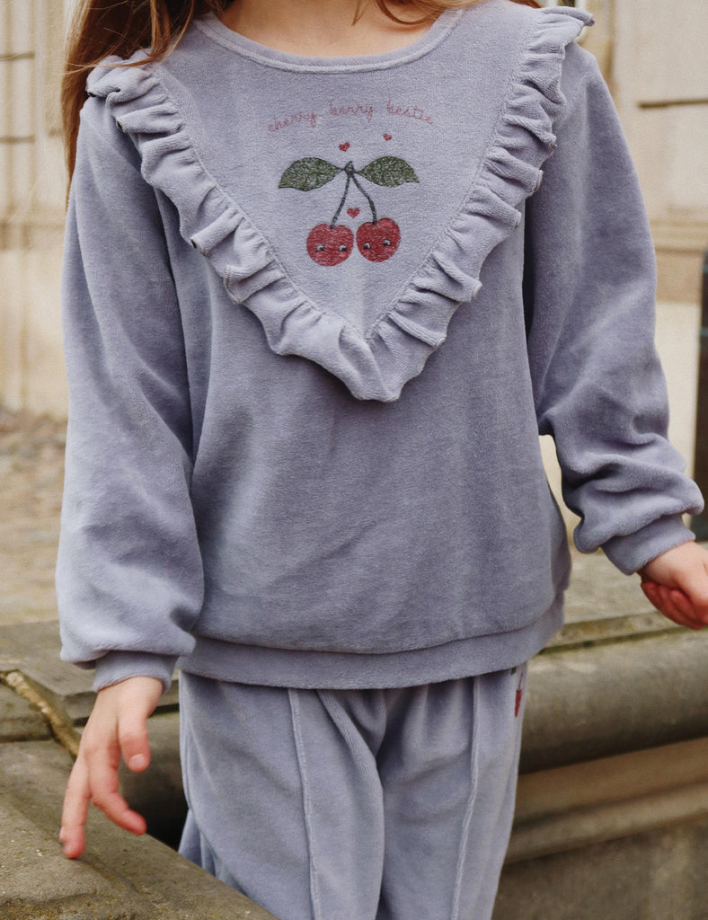 Child wearing a gray outfit with ruffled collar and embroidered design outdoors.