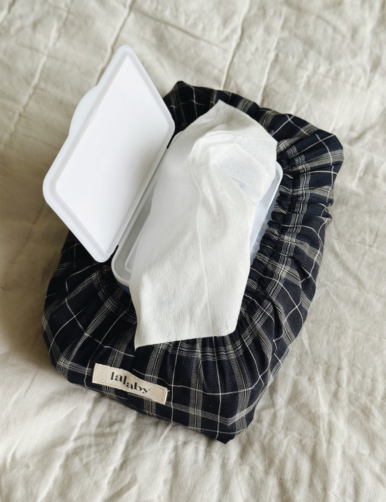 Black and white checkered bag with white wipes and a white container on a beige fabric background