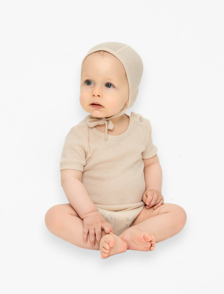 Image of a 9 month old infant sitting up wearing the wool silk bonnet in buttercream and matching onesie.