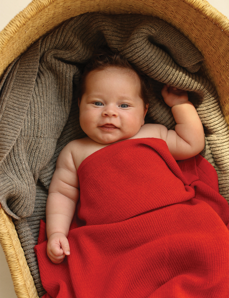 Baby wrapped in a red blanket lying on a textured surface