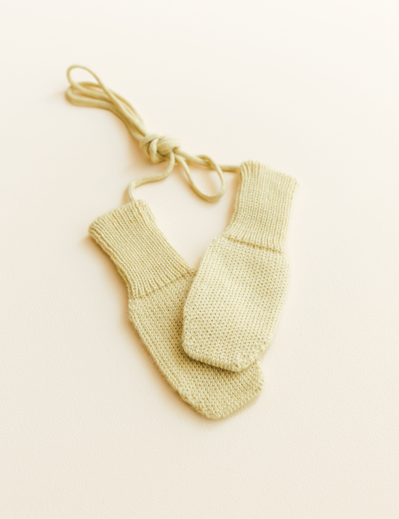 Pair of yellow knitted baby mittens on a beige background