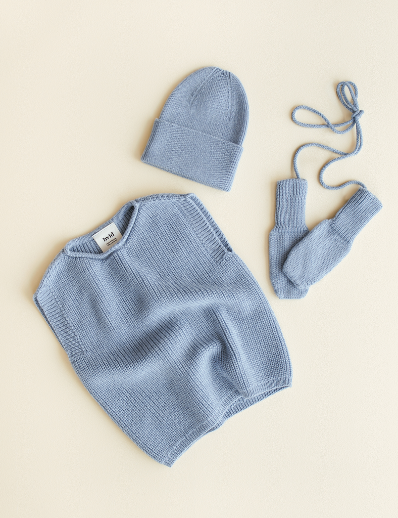 Blue baby sweater, hat, and booties on a beige background