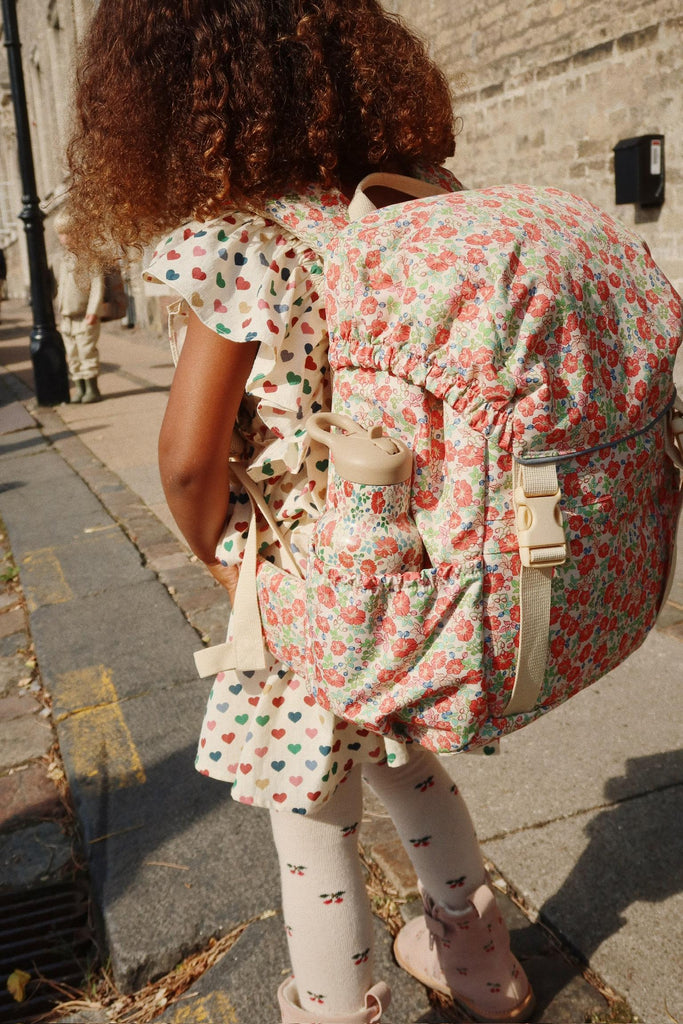 Child wearing a floral dress and backpack on a sidewalk